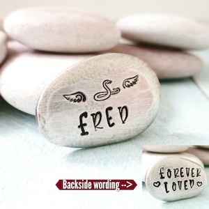May include: A silver-colored stone with the name "FRED" engraved on it, along with a snake with wings. The back of the stone has the words "FOREVER LOVED" engraved on it.