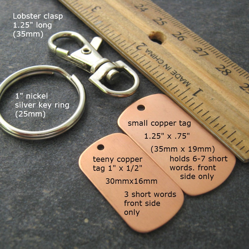 May include: Two copper tags with text on them. The larger tag is 1.25 inches by .75 inches and says "small copper tag 1.25" x .75" (35mm x 19mm) holds 6-7 short words. front side only". The smaller tag is 1 inch by 1/2 inch and says "teeny copper tag 1" x 1/2" 30mmx16mm 3 short words front side only".