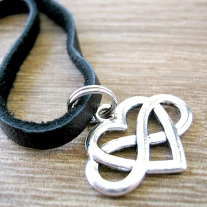 May include: A silver Celtic knot heart pendant on a black leather cord necklace.