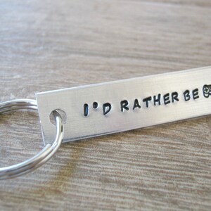 May include: Silver keychain with a rectangular tag that reads "I'd rather be" with a video game controller icon.