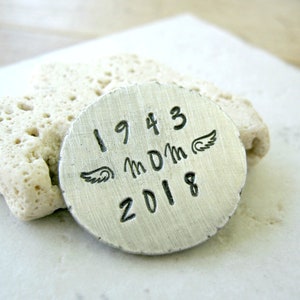 May include: A silver metal disc with the dates 1943 and 2018, the letters "MDM" and two angel wings.