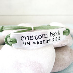 May include: A green suede bracelet with a silver metal tag that says "custom text on both sides".