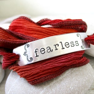 May include: A silver bracelet with the word "fearless" engraved on it. The bracelet is wrapped in a red ribbon.