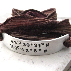 May include: A silver bracelet with a brown ribbon. The bracelet has coordinates engraved on it: 43.0 39° 21" N 110.0 43° 6" W.