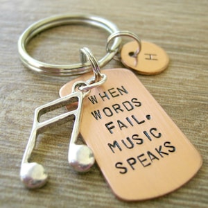 May include: A copper keychain with a silver music note charm. The keychain has the text "When words fail, music speaks".