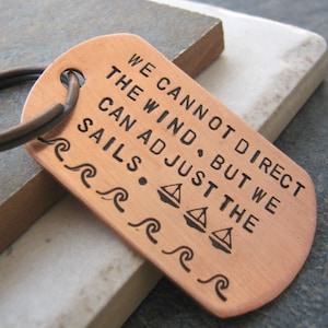 May include: Copper keychain with the quote "We cannot direct the wind, but we can adjust the sails."  The quote is surrounded by a border of stylized waves.