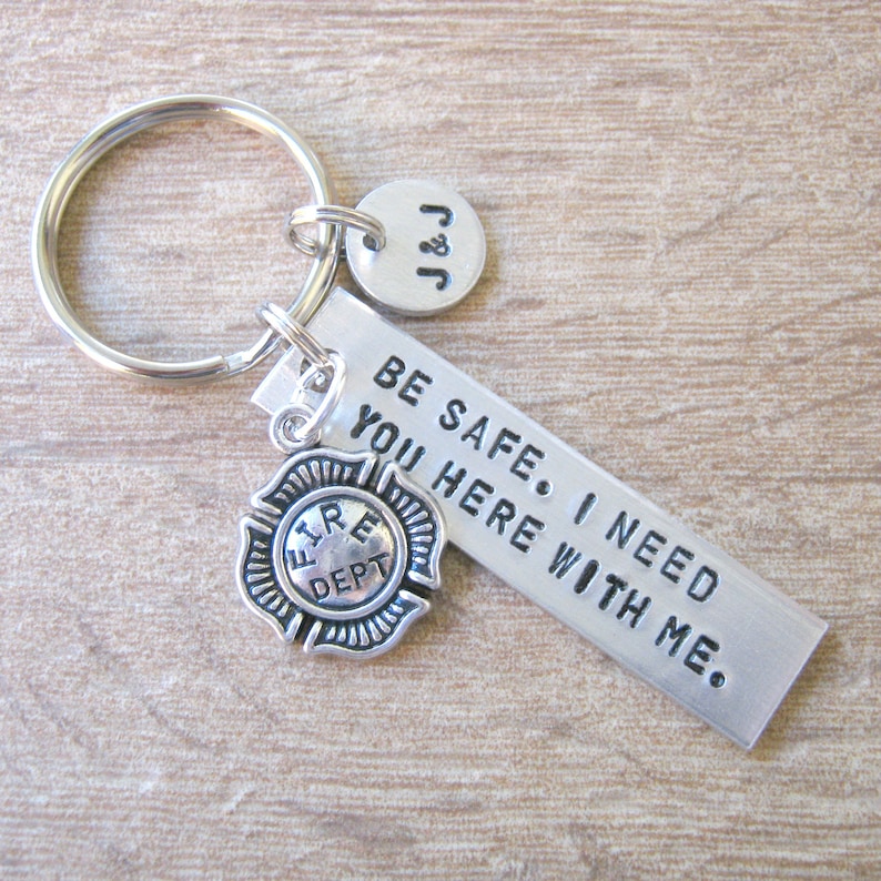 May include: Silver keychain with a firefighter charm, a small tag with the text "J&J" and a larger tag with the text "BE SAFE. I NEED YOU HERE WITH ME."
