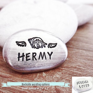 May include: A silver-colored stone engraved with the name "HERMY" in black, with a decorative design above the name and wings on either side. The stone measures 1.5" x 1".