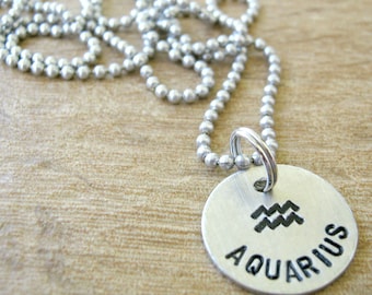 May include: Silver chain necklace with a round silver pendant that says "Aquarius" with the Aquarius astrological symbol.