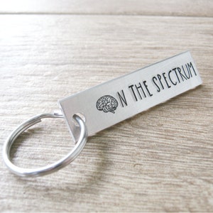 May include: Silver keychain with a brain graphic and the text "On the Spectrum".