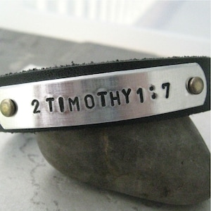 May include: A black leather bracelet with a silver metal plate engraved with the text "2 Timothy 1:7".