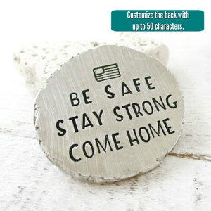 May include: A silver metal disc with a distressed finish, featuring the text "BE SAFE STAY STRONG COME HOME" and a small American flag icon. The back of the disc can be customized with up to 50 characters.