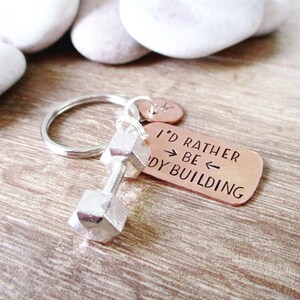 May include: A silver dumbbell keychain with a copper tag that reads "I'd rather be body building".