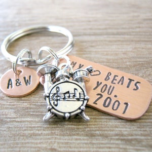 May include: A silver charm of a drum set with a music note on the bass drum is attached to a copper keychain with the text "My Beats You 2001" and a copper charm with the text "A&W".