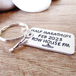 May include: Silver key chain with a silver oar charm. The tag reads "HALF MARATHON FEB 2023 ROW HOUSE FM" with a small rowing boat graphic.