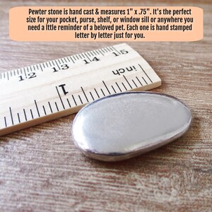 May include: A silver pewter stone measuring 1 inch by 0.75 inches. The stone is next to a wooden ruler with inch markings.