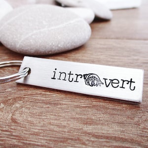 May include: A silver keychain with a black inscription that reads "introvert" and a small hermit crab graphic.