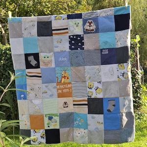 May include: A patchwork quilt made of various blue, gray, and white fabric squares featuring cartoon characters, stripes, and text including "precious cargo," "Julek," "100% UNIQUE," and "PRZYSTOJNY JAK TATA :)" hanging from a clothesline.