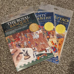 Peut inclure: Trois ensembles de transferts à frotter, intitulés "The Royal Banquet", "Knights' Tournament" et "Attack". Chaque ensemble présente une scène médiévale avec des illustrations de personnes, de nourriture et d'action. L'emballage contient du texte et des illustrations.