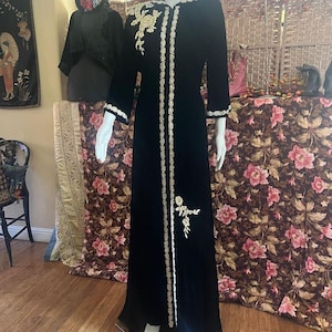 May include: A long black velvet robe with gold embroidery and a stand-up collar. The robe has a long, flowing silhouette and is adorned with intricate floral designs.