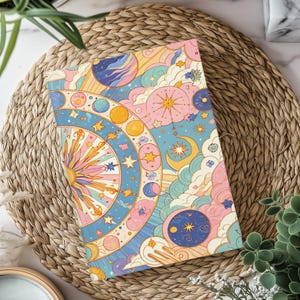 May include: A rectangular notebook featuring a vibrant celestial illustration with a central sunburst, concentric circles of planets, stars, a crescent moon, and fluffy clouds in a pastel color palette of pink, blue, yellow, and orange.