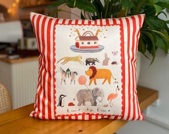 May include: Square cushion with a red and white striped border. The central design features a colourful illustration of animals like a zebra, lion, and elephant, with the words "two by two" at the bottom. The background is off-white.