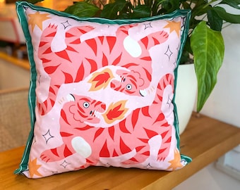 May include: Square cushion featuring a pink background with a repeating pattern of red tigers. The tigers have orange flames and are outlined in red. The cushion has a green border.