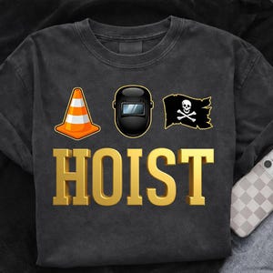May include: Dark gray sweatshirt with the word "HOIST" in gold block letters. Above the word are three graphics: an orange traffic cone, a black welding mask, and a pirate flag with a skull and crossbones.