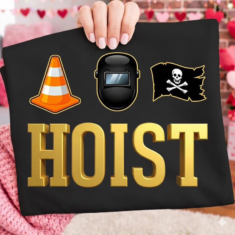 May include: Black t-shirt with gold 3D text that reads "HOIST". The shirt features three graphics: an orange and white traffic cone, a black welding mask, and a pirate flag with a skull and crossbones.