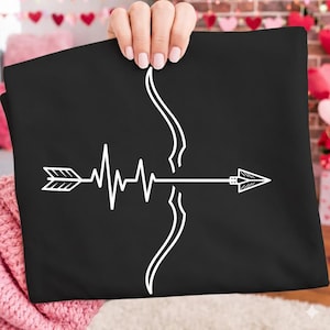 May include: Black t-shirt featuring a white graphic of a bow and arrow with a heartbeat design. The arrow is positioned horizontally, with the bow's curve on the right side. The design is simple and modern.