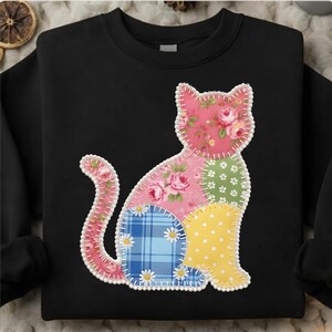 Puede incluir: Sudadera negra con un diseño de gato patchwork. El gato está compuesto por varios patrones de tela, incluyendo floral, lunares y cuadros, en tonos rosa, verde, azul y amarillo. El contorno del gato está cosido con hilo blanco.