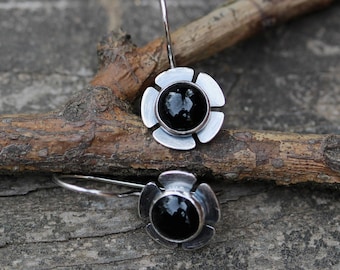 May include: A pair of silver earrings with black gemstone accents. Each earring features a flower-shaped design with five petals.