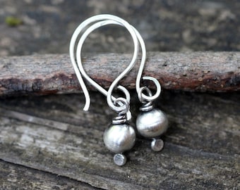 May include: A pair of silver dangle earrings with small round beads. The earrings have a simple, minimalist design.