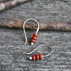 May include: A pair of silver dangle earrings with three red beads on each earring.