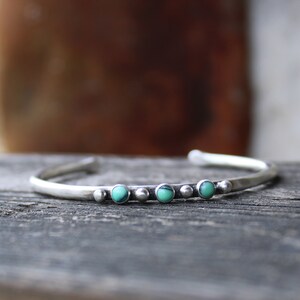 May include: A silver bracelet with a row of turquoise stones set in a hammered metal band.