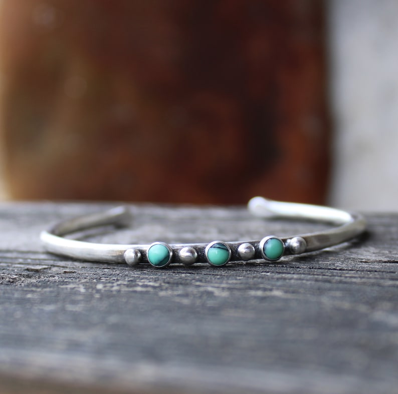 May include: A silver bracelet with a row of turquoise stones set in a hammered metal band.