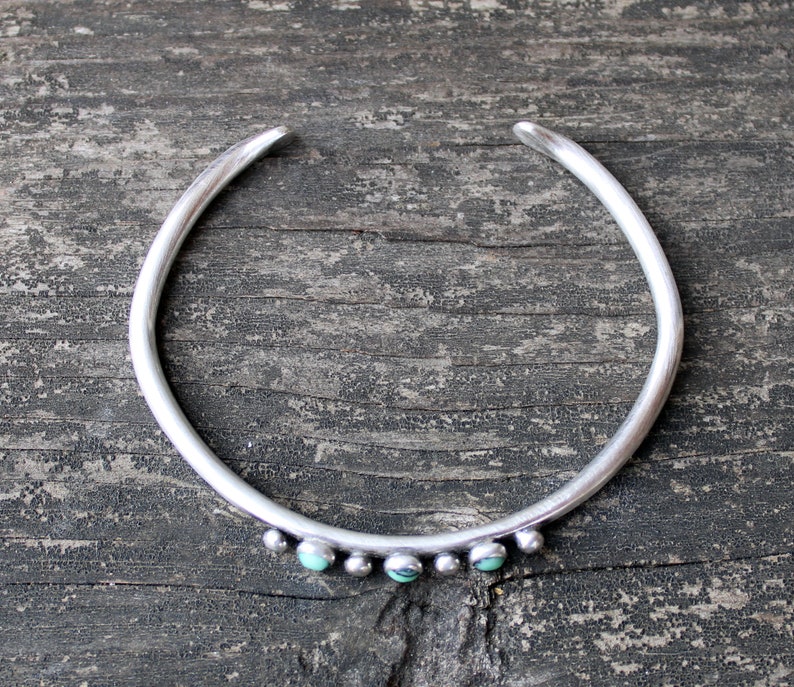 May include: A silver bangle bracelet with turquoise stones set in the metal. The bracelet is open and has a simple design.