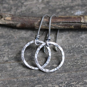 May include: A pair of silver dangle earrings with hammered circular pendants. The earrings have a simple, minimalist design.