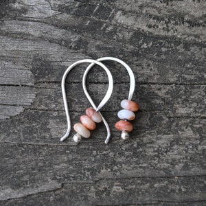 May include: A pair of silver earrings with three stacked, oval-shaped, pink and white stones.