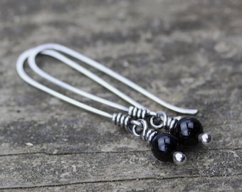May include: A pair of silver dangle earrings with black gemstone beads. The earrings are made with thin silver wire and have a simple design.