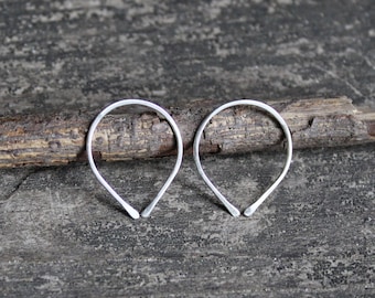 May include: A pair of silver hoop earrings with a teardrop shape. The earrings are on a wooden surface.