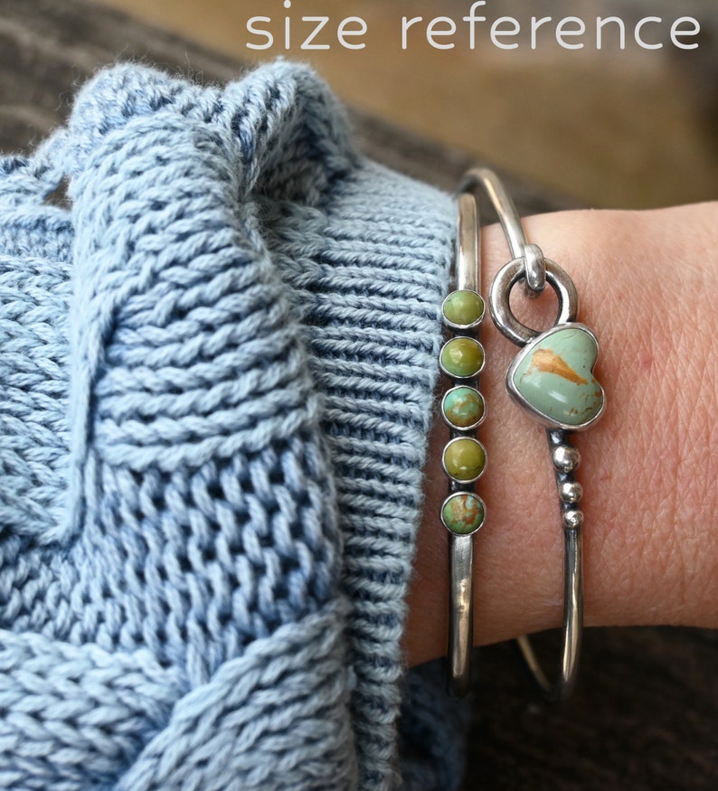 Pode incluir: Duas pulseiras de prata. Uma tem cinco pedras de turquesa verde. A outra tem uma pedra de turquesa em forma de cora&ccedil;&atilde;o. As pulseiras s&atilde;o usadas sobre um su&eacute;ter de malha azul claro. O texto "size reference" est&aacute; no topo.