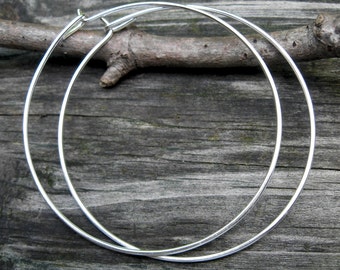 May include: A pair of silver hoop earrings. The hoops are large and circular, and they are made of a thin metal.