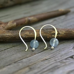 May include: A pair of dangle earrings featuring curved silver-toned metal hooks. Each earring is accented with a single, translucent, pale blue spherical bead and a small, polished silver-toned metal ball at the base of the hook.