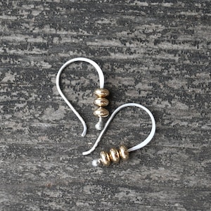May include: A pair of silver hoop earrings with gold beads. The earrings are simple and elegant, and would make a great gift for any occasion.