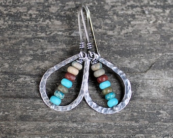 May include: A pair of silver teardrop-shaped earrings with a hammered texture, each featuring a strand of turquoise and brown gemstone beads.