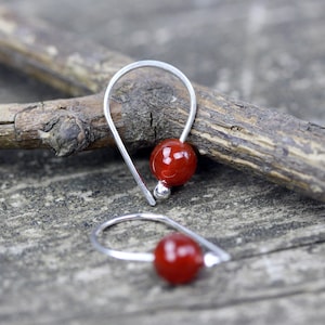 May include: A pair of silver hoop earrings with a red gemstone bead on each hoop.