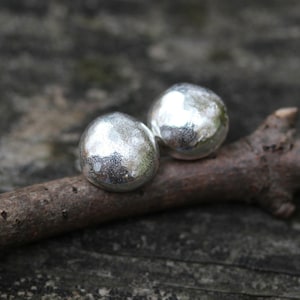 May include: A pair of silver earrings with a hammered texture. The earrings are round and have a smooth, polished finish.