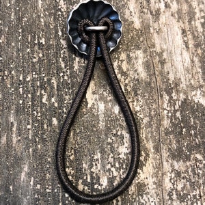 May include: A black elastic band with a silver metal loop, attached to a silver metal disc with a scalloped edge.