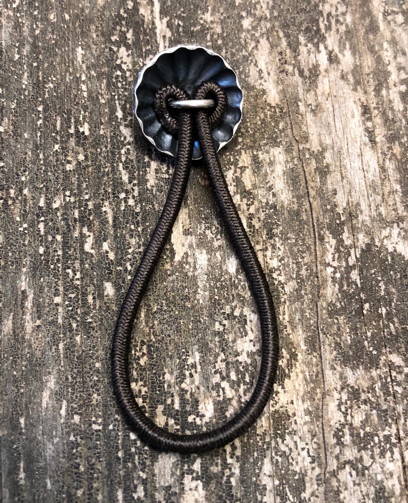 May include: A black elastic band with a silver metal loop, attached to a silver metal disc with a scalloped edge.